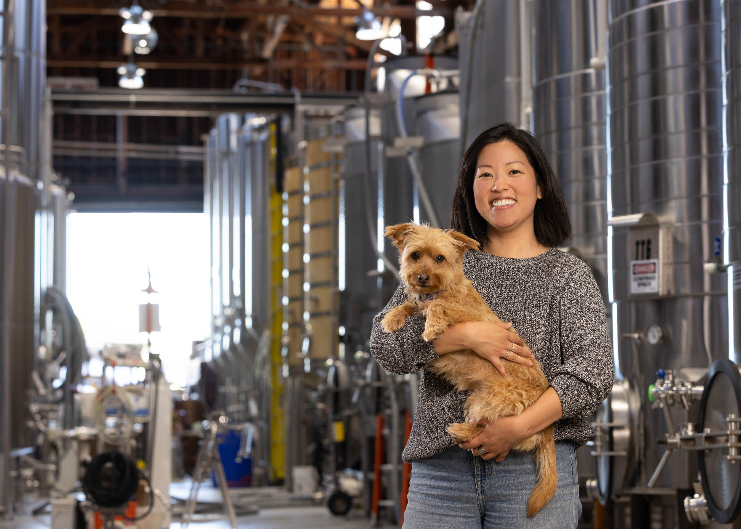 smiling-asian-woman-holding-scruffy-small-dog-at-beer-brewery-3716
