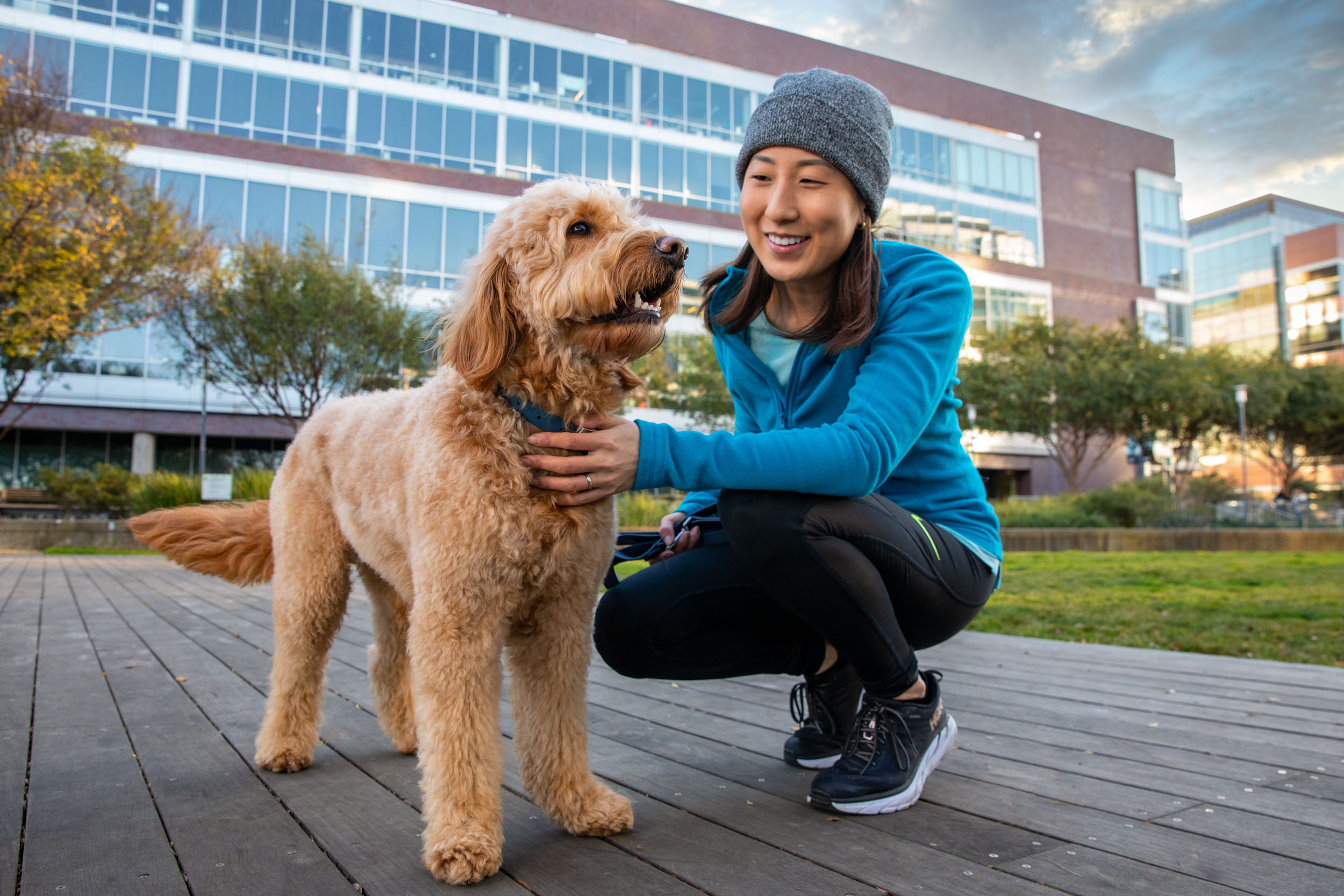 Asian Woman in Hat Next to Goldendoodle in City Park